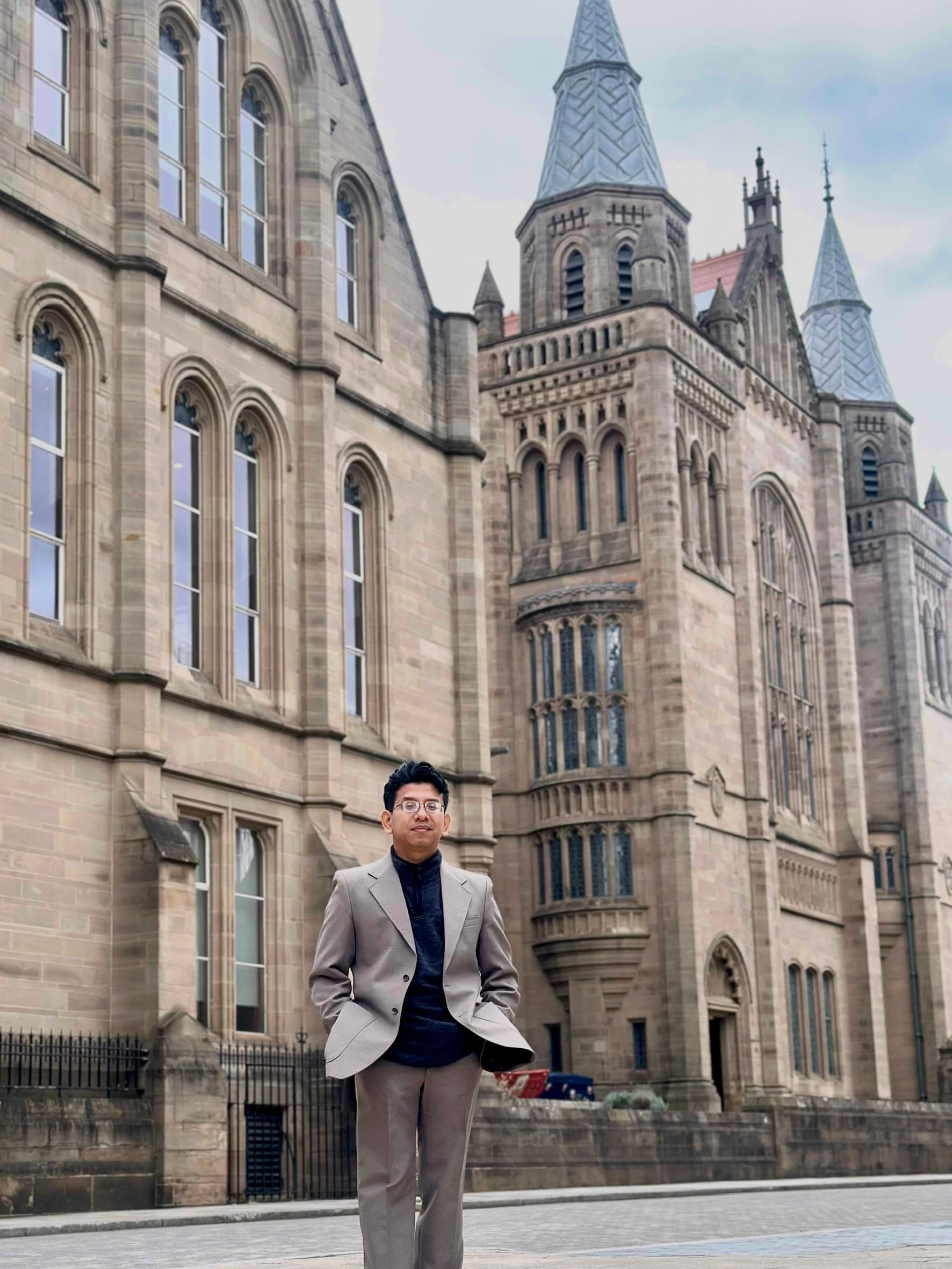 Man in a tan suit stands before a grand Gothic-style stone building with spires.
